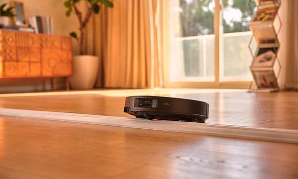 Svart robotstøvsuger kjører over dørterskel i stue