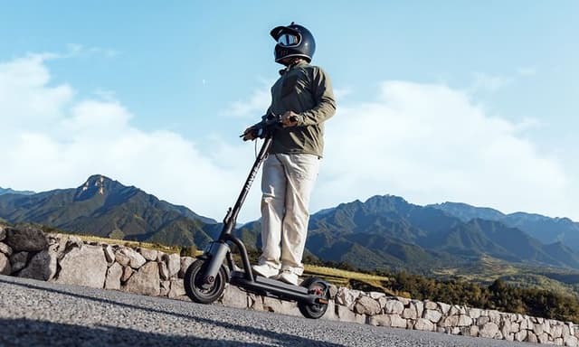 Henkilö ajaa loivaa mäkeä ylös sähköpotkulaudalla kypärä päässään