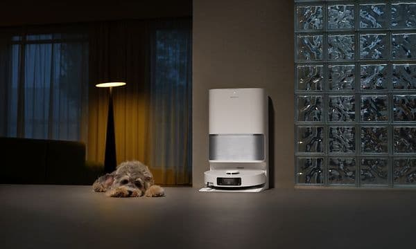 Robotstøvsuger står dokket i ladestasjon ved siden av hund