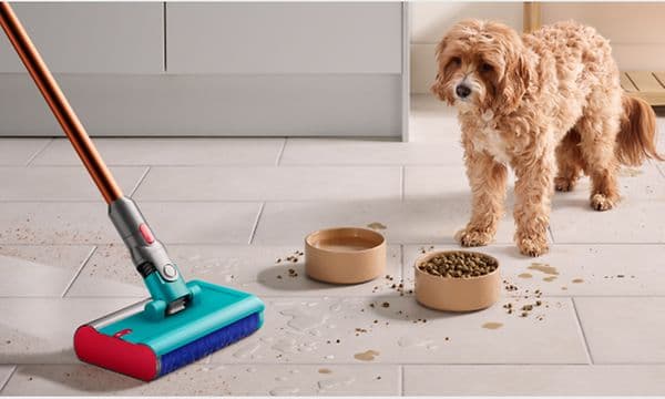 Dyson V10 Submarine-støvsuger rengjør søl fra hundeskåler på kjøkkengulv mens hund ser på