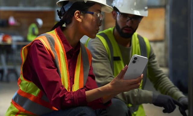 Apple - B2B - Two people in reflective vests and helmets looking at an iPhone 17