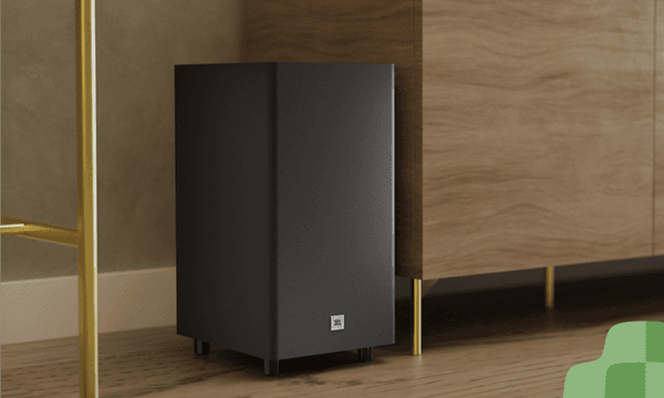 JBL trådløs subwoofer på gulvet ved siden af et møbel
