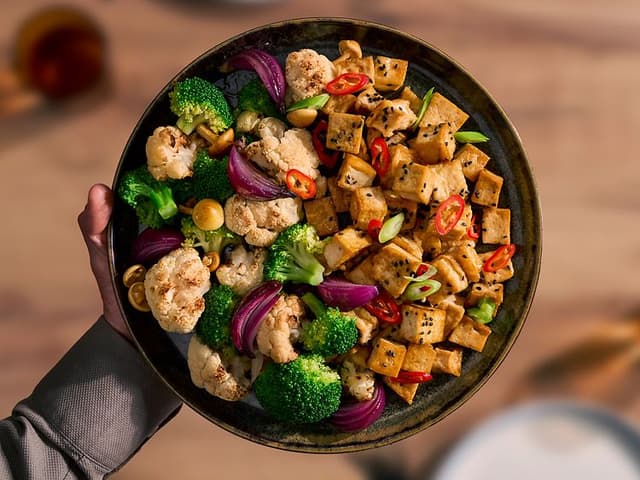 Nærbillede af en skål med tofu, broccoli og blomkål, klar til at blive spist