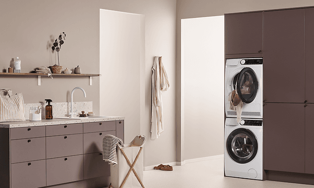Valkoinen pesukone ja kuivausrumpu asennettuna pesutorniksi kodinhoitohuoneen kaapistoon