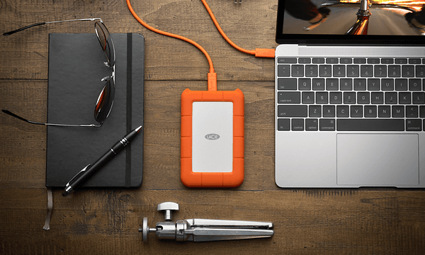 Lujatekoinen LaCie Rugged Mini SSD -levy kannettavan tietokoneen ja muiden tarvikkeiden kanssa pöydällä