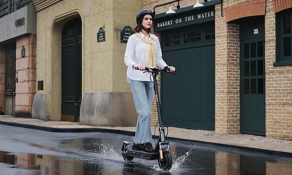 Kvinne kjører en Navee GT5 Max elektrisk sparkesykkel på våt asfalt