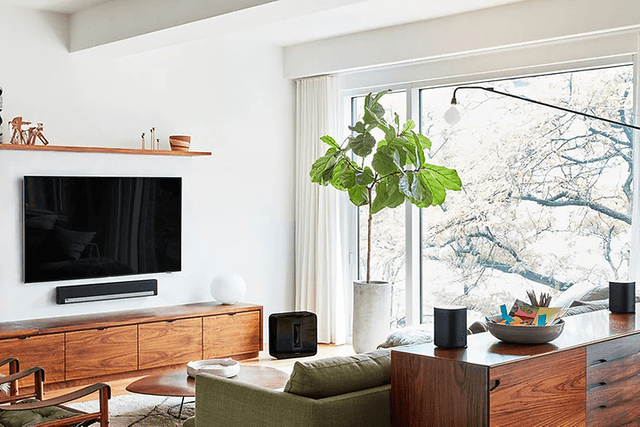 Modernt vardagsrum med platt-TV på väggen, soundbar under och flera smarta högtalare runt om i rummet.