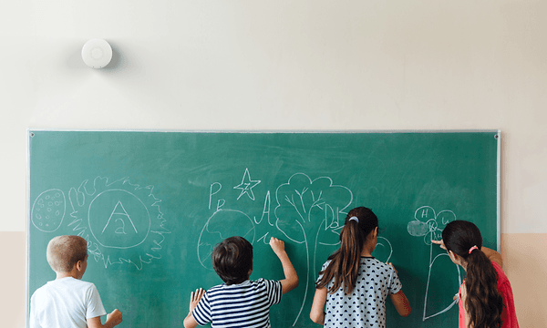 Airthings Wave on a class room wall over a chalkboard where kids are making drawings