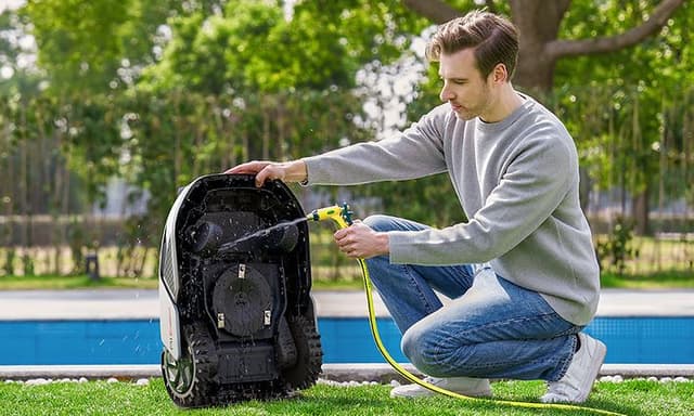 Mies huuhtelee Dreame A1 Pro 800 -robottiruohonleikkurin pohjaa puhtaaksi pihallaan