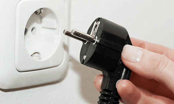 Närbild på en hand som sätter i en svart kontakt i ett eluttag. 