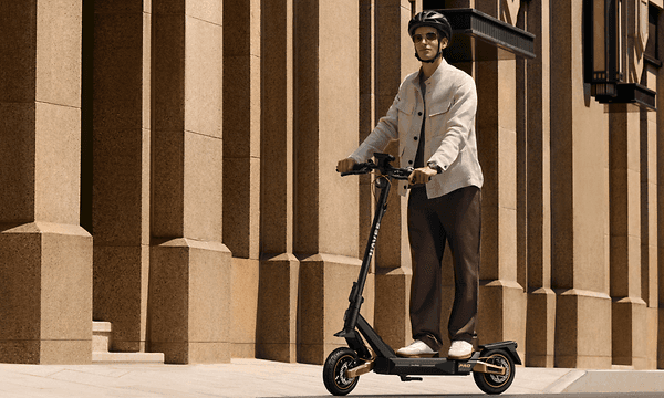 Man åker på sin Navee ST5 Pro elsparkcykel längs en beige byggnad