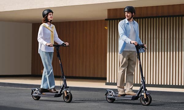 En man och en kvinna kör varsin Navee GT5 Max elsparkcykel på en tom gata