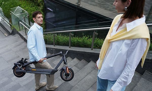 Mies kantamassa taitettavaa Navee GT5 Max ‑sähköskootteriaan ulkoportaita ylös