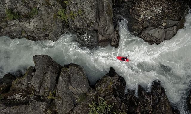 En person som paddlar kayak i en fors omringad av berg