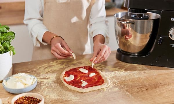 Nainen lisää juustoa tomaattikastikkeella päällystetyn pizzataikinan päälle