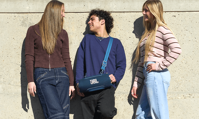 Tre vänner lutar mot en solig vägg, en bär en JBL Xtreme 5 högtalare med en axelrem