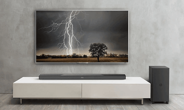 Stor TV uppsatt på väggen med bild på en åskblixt. Tillhörande högtalare vid sidan och soundbar placerad på en vit TV-bänk.