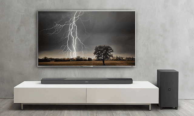 Stor TV uppsatt på väggen med bild på en åskblixt. Tillhörande högtalare vid sidan och soundbar placerad på en vit TV-bänk.