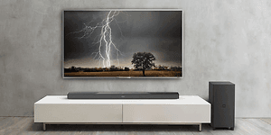Stor TV uppsatt på väggen med bild på en åskblixt. Tillhörande högtalare vid sidan och soundbar placerad på en vit TV-bänk.