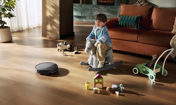 Et barn leker i stuen mens Roborock Saros 20 støvsuger gulvet.