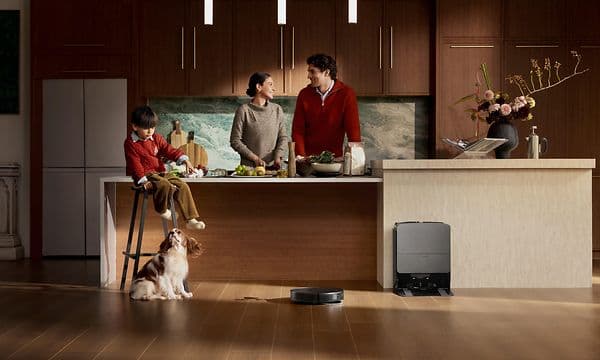 En familie lager mat på kjøkkenet mens Roborock Saros 20 vasker søl på gulvet.