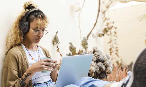 Kvinde, der arbejder på sin computer udendørs, mens hun har høretelefonerne på