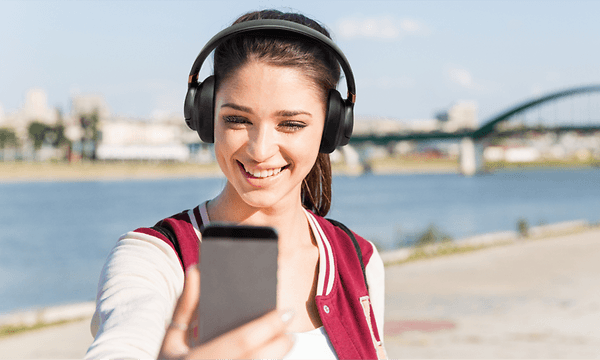 Nainen puhuu facetime-puhelua ulkona kuulokkeet päässään