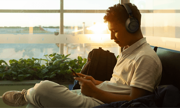 Man sitter på en flygplats och tittar på telefonen och bär hörlurar