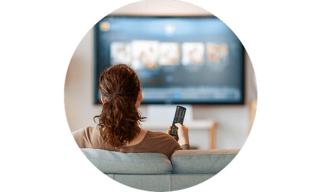 Nainen istuu sohvalla katselemassa televisiota
