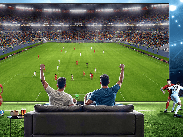 TV-skjerm på stadion og to menn som ser på den fra sofaen