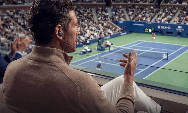 Mies puhuu puhelua Liberty 5 Pro Max -nappikuulokkeilla hälyisässä tenniskilpailun katsomossa