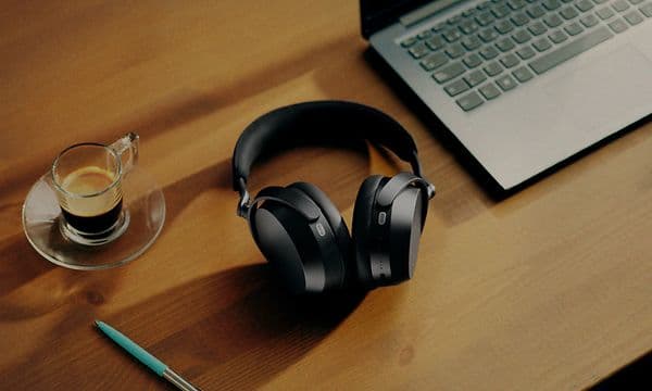 Svarta Momentum 5 hörlurar på ett skrivbord i trä mellan en laptop, en kopp espresso och en penna.