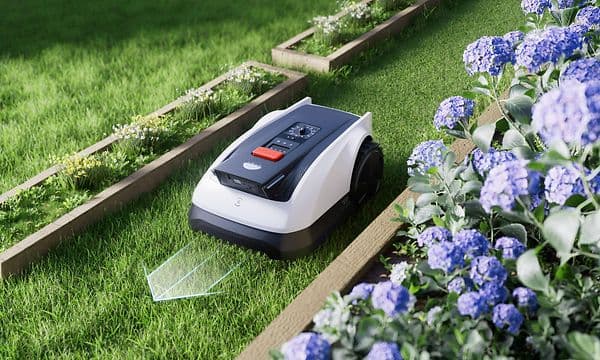 En Ecovacs Goat O800 RTK klipper gräsmattan i en smal passage mellan en örtträdgård och en blomlåda.