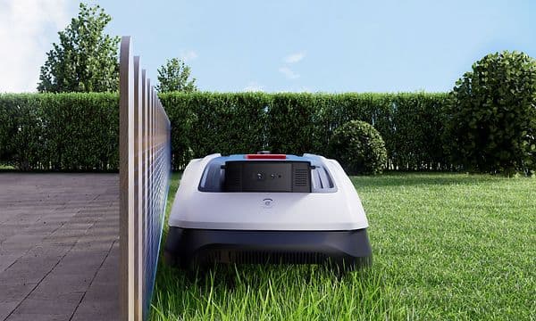 En Ecovacs Goat O800 RTK klipper gräsmattan nära ett vitt staket med TruEdge-precision.