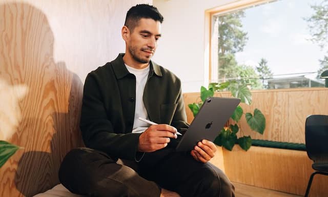 Man som sitter på en träbänk och jobbar med sin Apple iPad