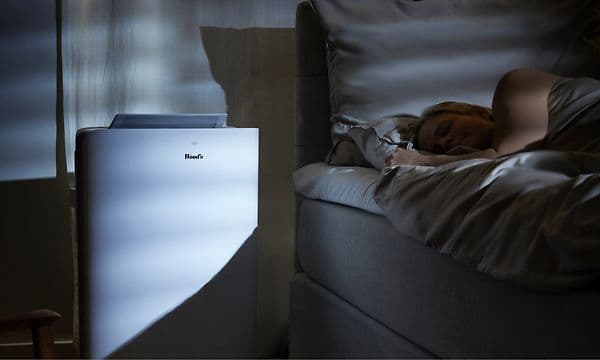 Et hvitt Wood's klimaanlegg på et mørkt soverom ved siden av en sovende kvinne.