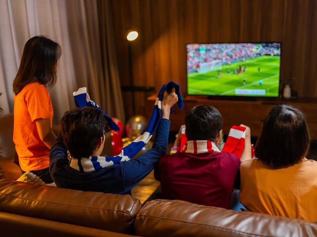 Familie sidder i sofaen og ser fodbold på tv