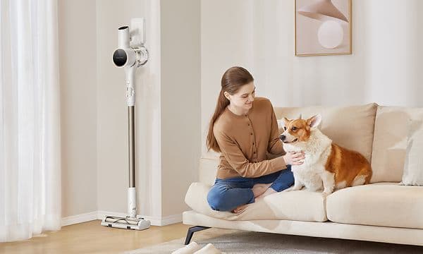 Kvinde sidder på en sofa med en hund og Dreame R10S NE ved siden af