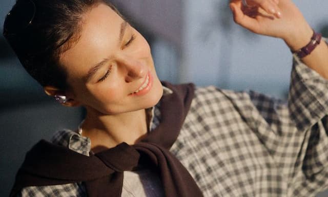 En ung, leende kvinna bär Sennheiser Momentum True Wireless 5-hörlurar utomhus.