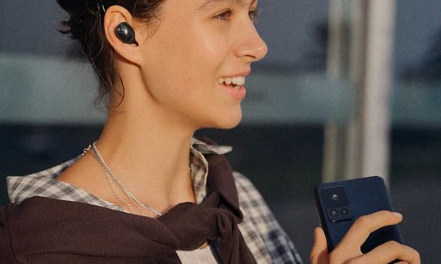 En ung, leende kvinna pratar i telefon medan hon bär Sennheiser Momentum True Wireless 5-hörlurarna.