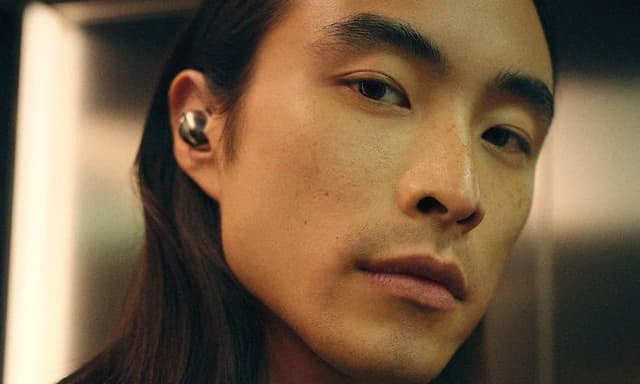 En ung man bär Sennheiser Momentum True Wireless 5-hörlurar och tittar in i kameran.