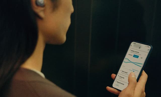 En person håller i en smartphone och justerar equalizern i appen.