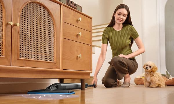 Dreame Mira Mop10 ja nainen joka siivoaa lattiaa puuhuonekalun alta koira vieressään