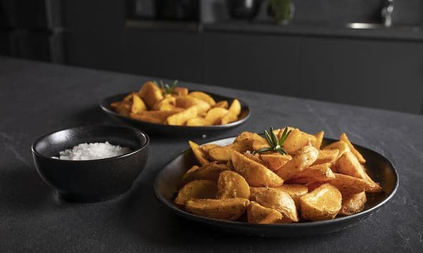 Svarta serveringstallrikar med airfryade potatisar tillagade i Hisense-pizzaugnen.