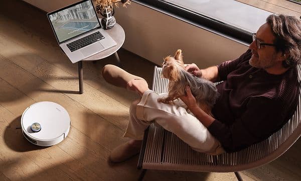 Mand sidder i en stol med en hund, mens Dreame L60 Pro Ultra gør rent