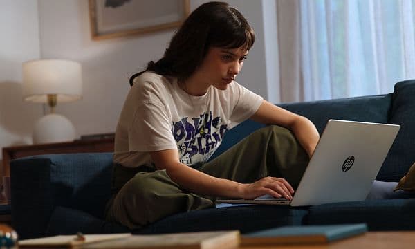 En kvinne sitter i en sofa foran en Omnibook 5 14-tommers AI-PC.