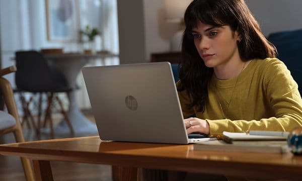 En kvinne sitter ved et skrivebord og arbeider på en Omnibook 5 14-tommers AI-PC.