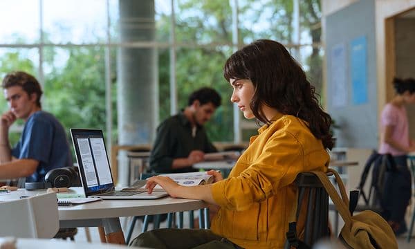 En kvinne sitter på et bibliotek ved et skrivebord med en Omnibook 5 14-tommers AI-PC.