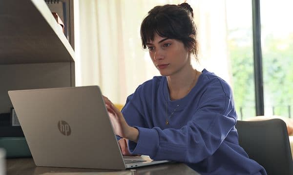 En kvinne sitter ved et skrivebord og berører Omnibook 5s 16-tommers skjerm med fingertuppene.