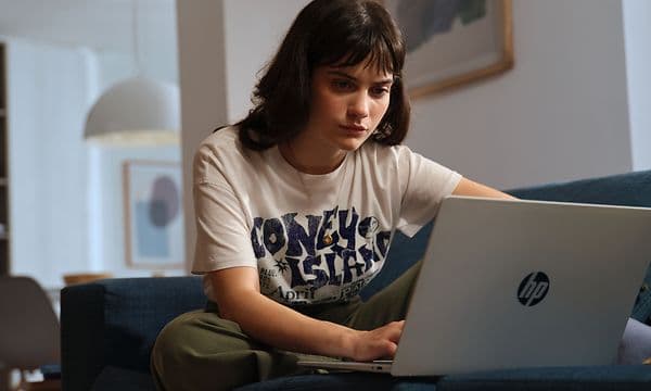 En kvinne sitter i en sofa foran en Omnibook 5 16-tommers AI-PC.